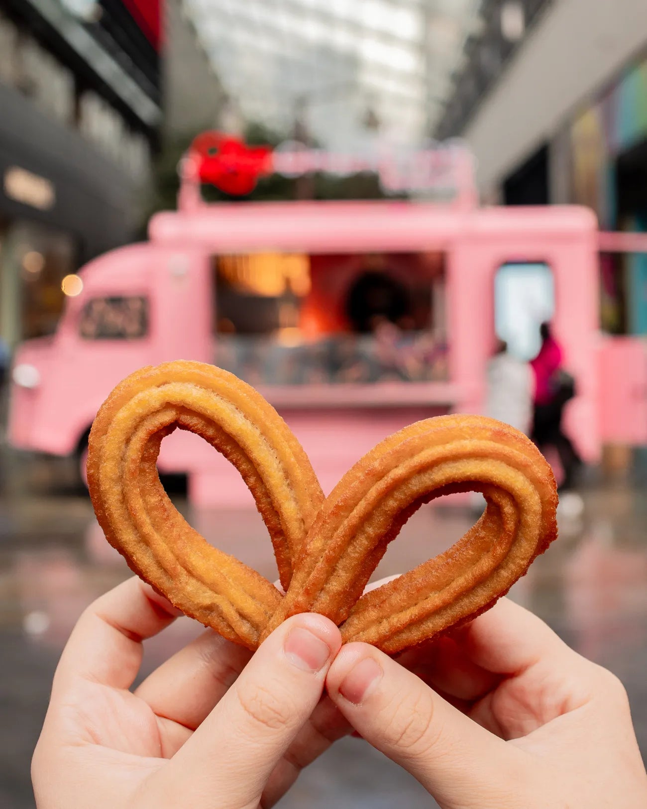 Two looped churros held together in front of the pink Love Churros van