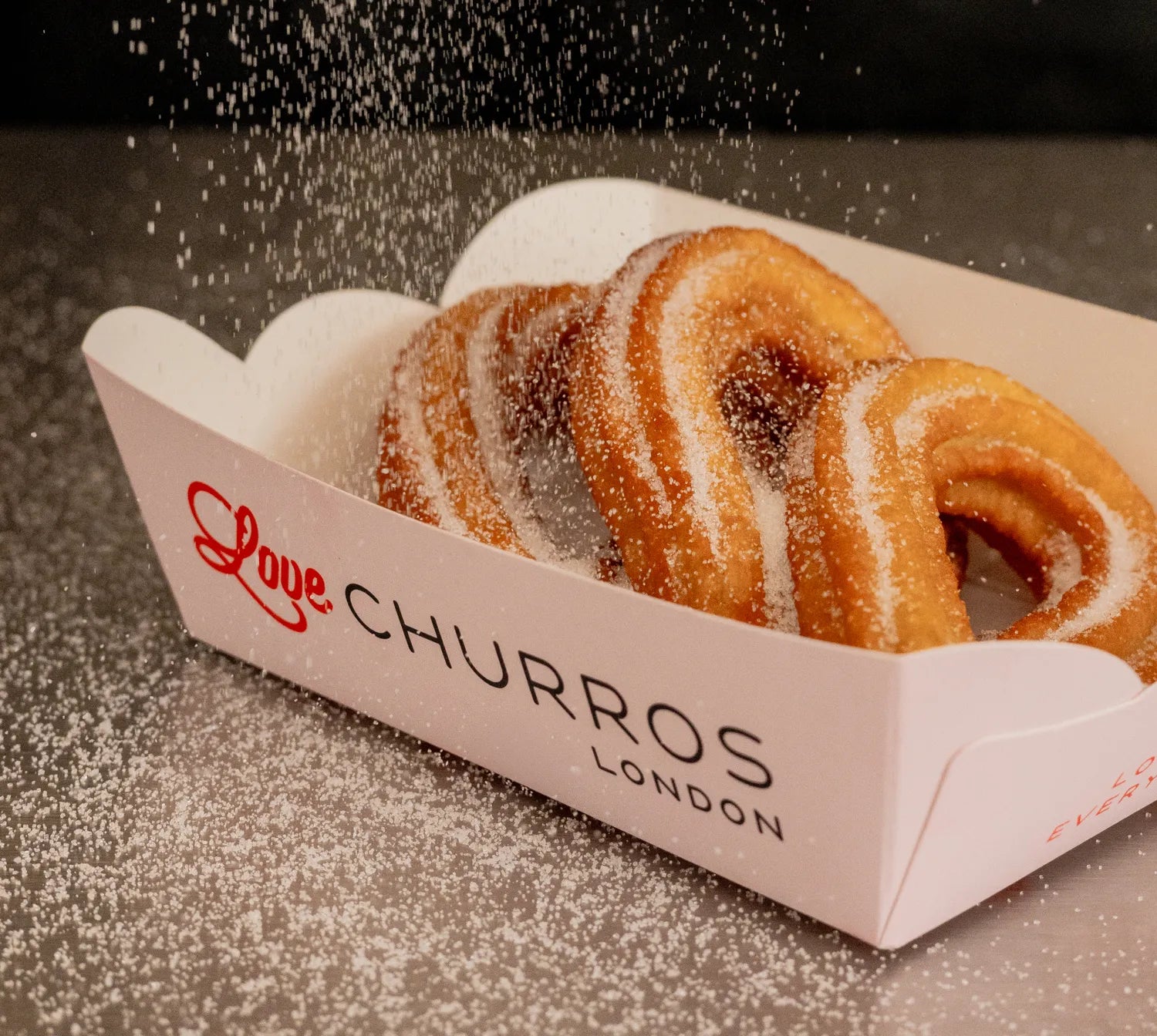 Looped churros dusted with sugar in a Love Churros tray